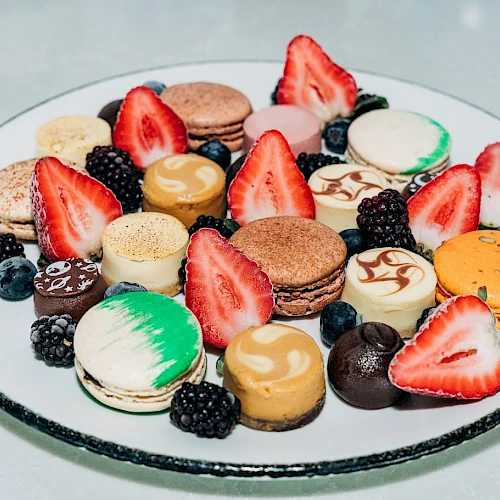 A fancy platter of assorted macarons, chocolate truffles, fresh strawberries, and berries arranged on a round plate.