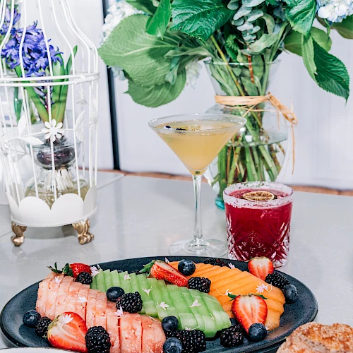 A vibrant breakfast spread featuring fruit-topped waffles and berries, with cocktails and fresh flowers in an elegant brunch setup.