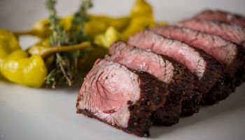 Sliced medium-rare beef roast with a dark crust, served with yellow mashed potatoes or puree and herbs on the side, stylish plate.