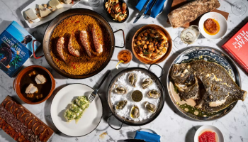 A festive feast with roasted chicken, stews, curries, breads, and small desserts arranged on a marble table, ready to share.