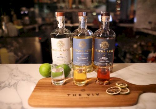 A whiskey tasting setup with three bottles and a shot glass on a wooden board, plus lime wedges and citrus garnishes on the board.