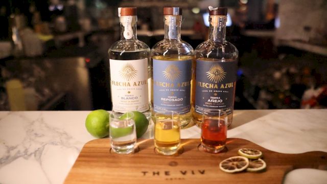 A whiskey tasting setup with three bottles and a shot glass on a wooden board, plus lime wedges and citrus garnishes on the board.