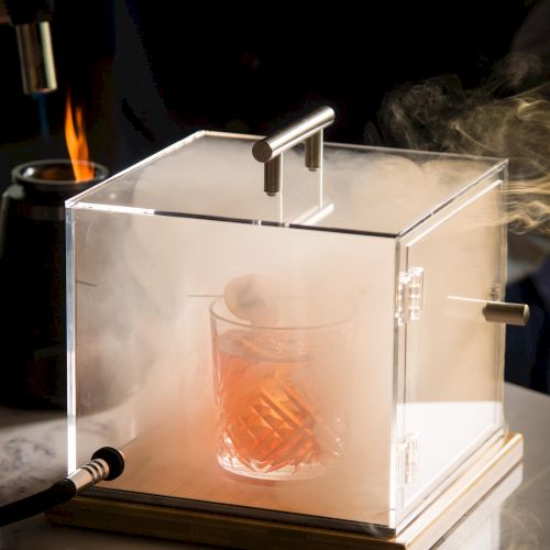 A small glass box with a red object inside, perched on a white base; a few metallic supports and a tiny plaque are nearby, under dim lighting.