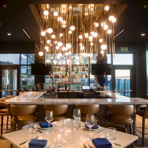 A stylish restaurant with warm lighting, a long wooden table set for a group, pendant lights, and a cozy ambiance.