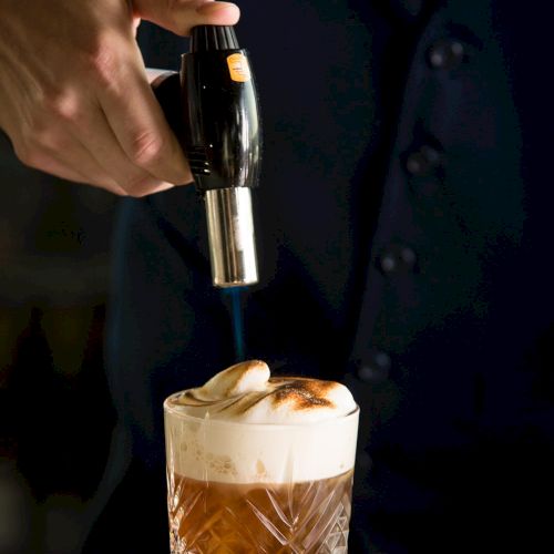 A close-up of a hand pouring a dark liquor from a bottle into a glass with ice, creating a layered cocktail. End.