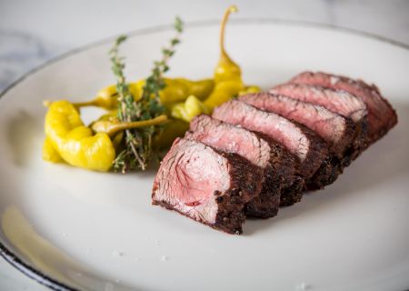 Sliced medium-rare steak with a mustard-yellow pur&eacute;e and herbs on the side, arranged neatly on a white plate for an elegant presentation.