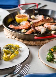 A fancy dining scene: grilled seafood skillet, roasted meat with greens, sliced beef, and wine on the table, all plated elegantly.