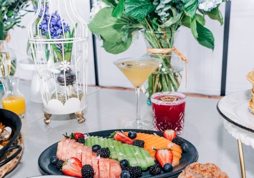 A vibrant breakfast spread featuring fruit-topped waffles and berries, with cocktails and fresh flowers in an elegant brunch setup.