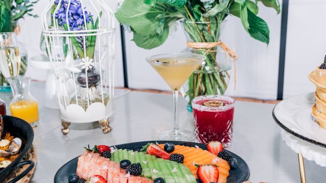 A vibrant breakfast spread featuring fruit-topped waffles and berries, with cocktails and fresh flowers in an elegant brunch setup.