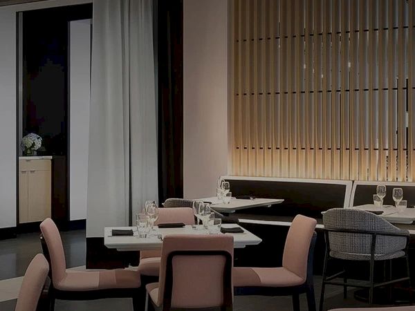 A modern restaurant dining area with neatly set tables, chairs, glassware, and warm wood slat walls.