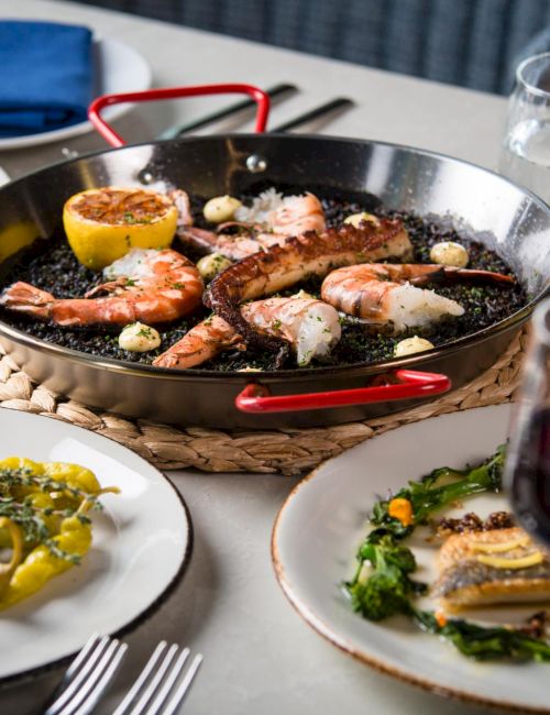 A sizzling skillet of shrimp and steak with lemon, served at a table with wine glasses and plates.