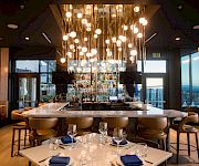 A modern restaurant/bar interior with glowing pendant globe lights, a back bar stocked with bottles, and dining tables set for guests.